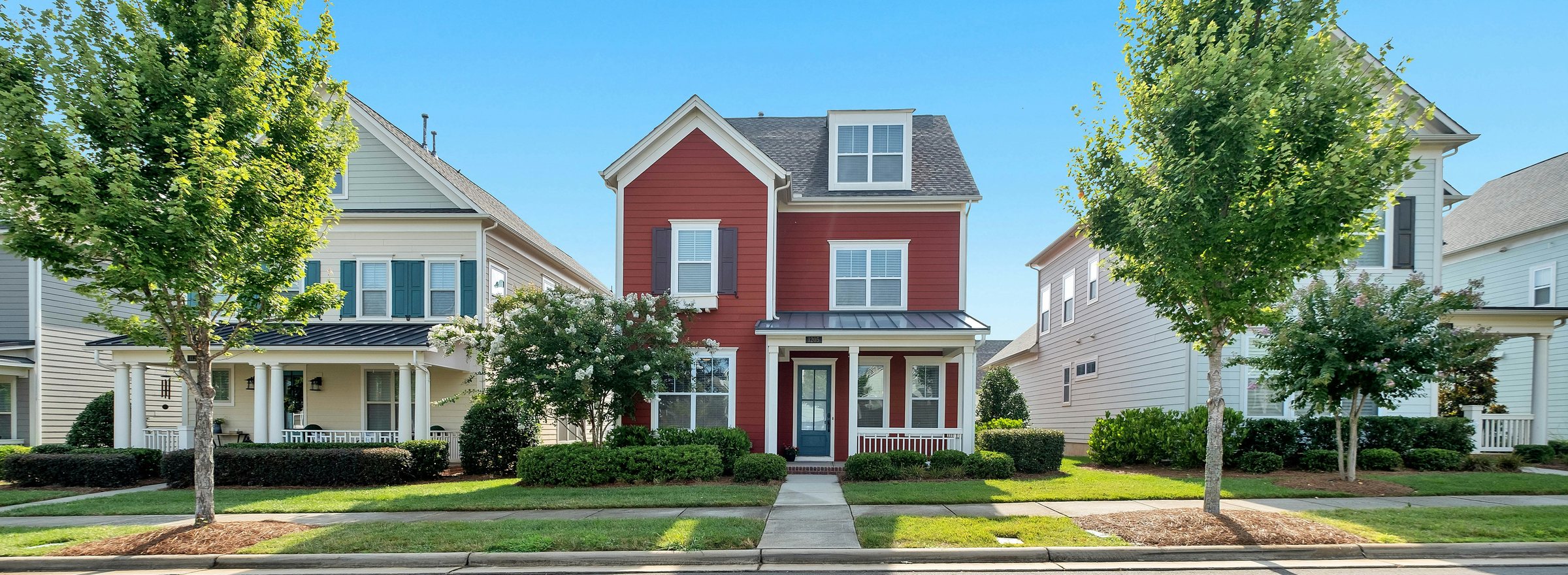 A red house with a white front porch on a leafy street