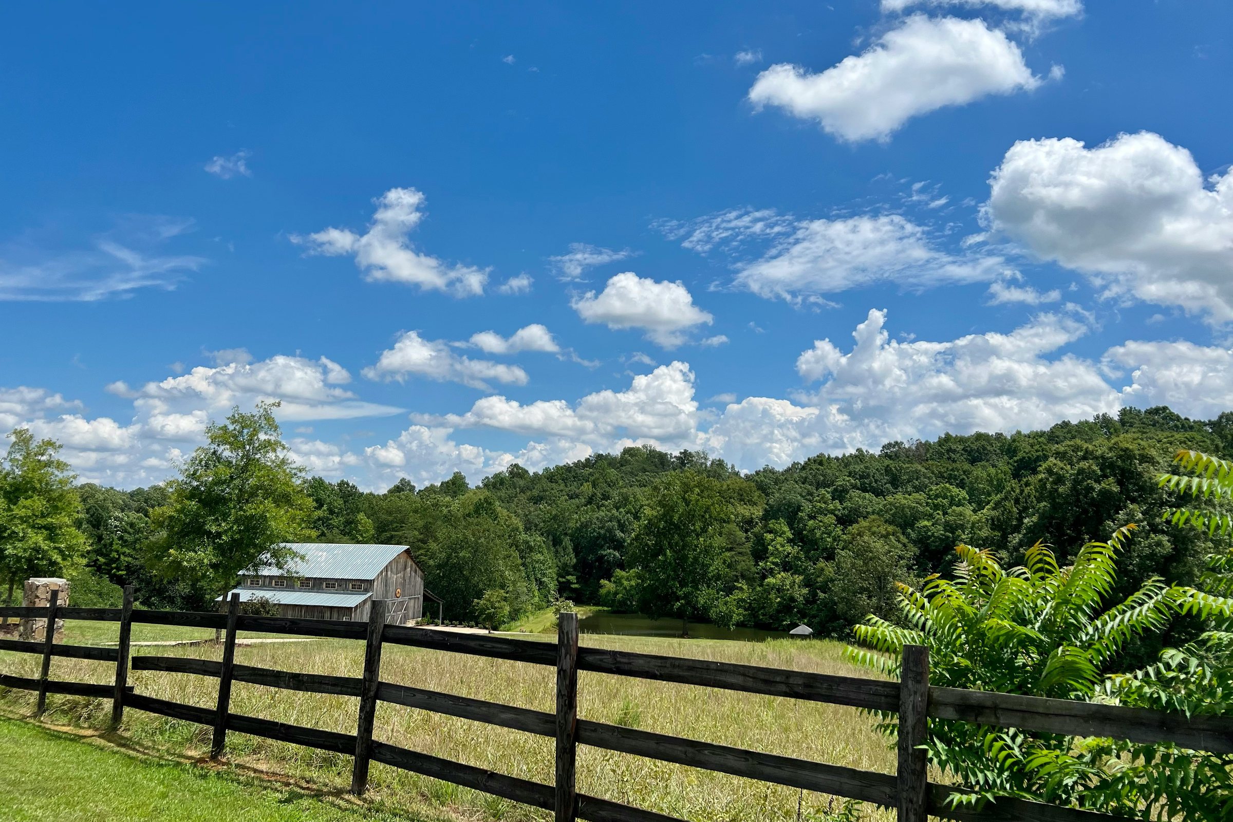 A split-rail fence, pasture and a barn under a blue sky