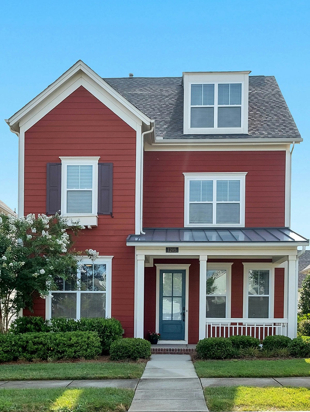 A red house with a white porch on a tree-lined street
